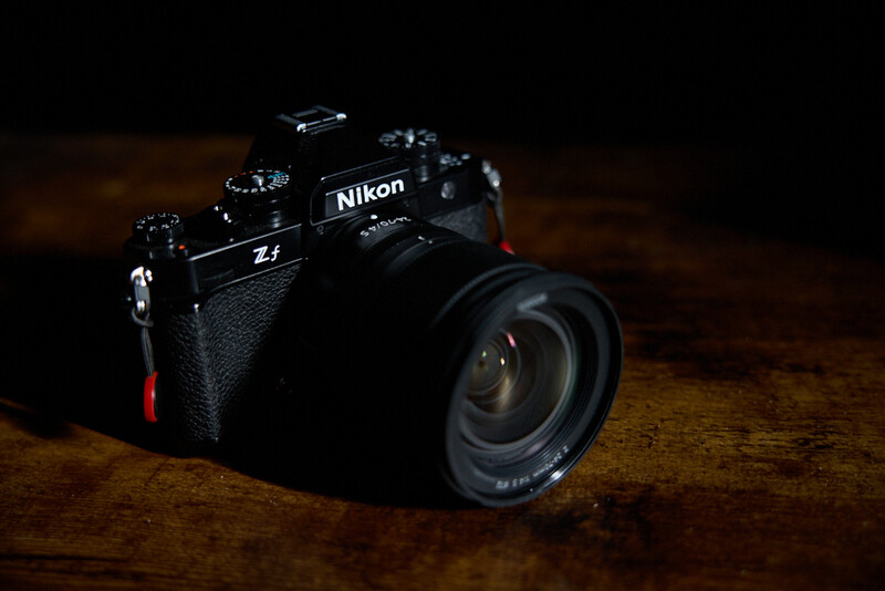 Nikon Z1 camera with attached lens on wooden surface, dramatically lit against dark background.