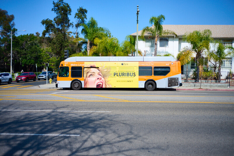 Yellow bus with large face graphic parked on sunny street with palm trees and residential buildings.