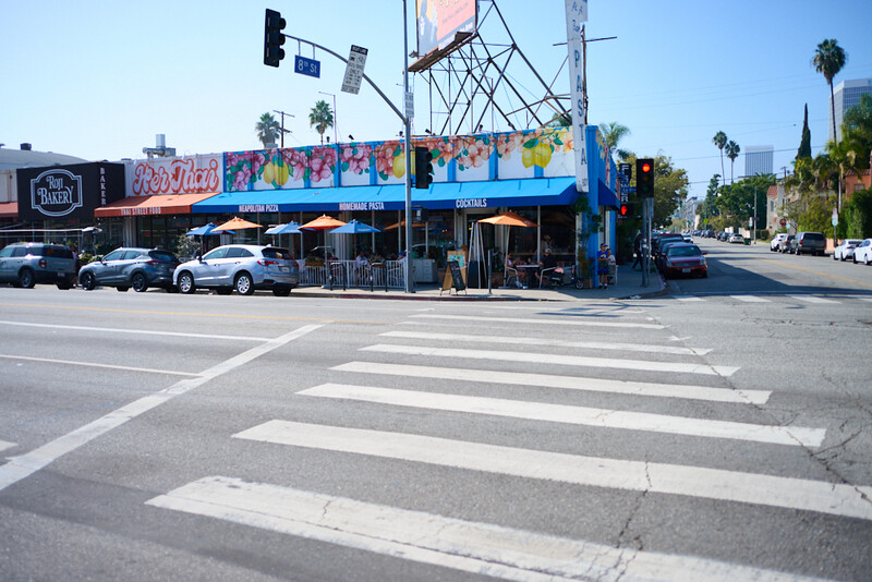 Pedestrian crosswalk with colorful storefronts and street infrastructure under bright daylight.