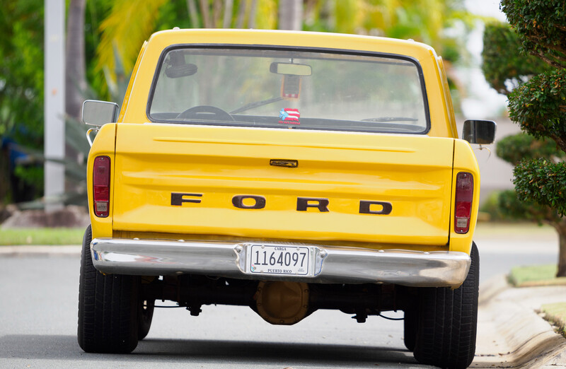 Rear view of a yellow Ford pickup truck parked on a residential street.