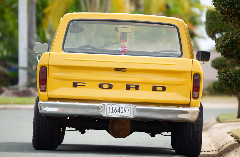 Rear view of a yellow Ford pickup truck parked on a residential street.