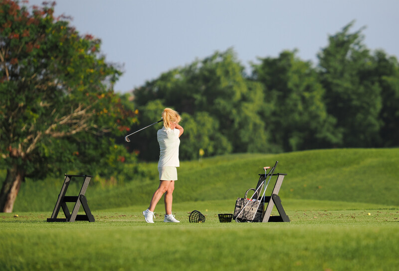 Young golfer mid-swing on a practice range with equipment arranged on either side.