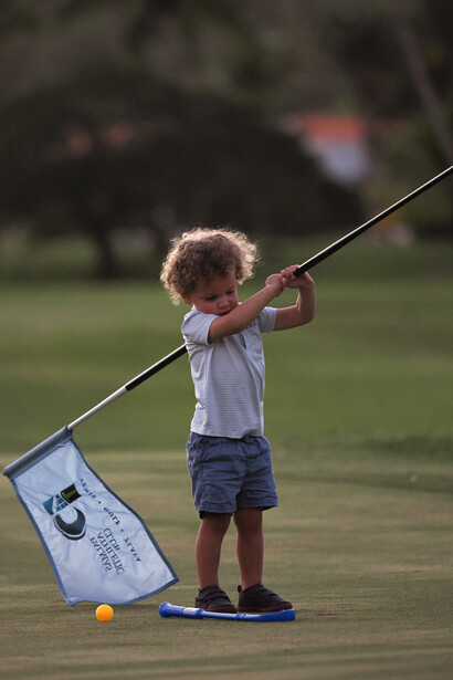 Young child with curly hair holding a fishing rod on a wooden dock, with a small bucket nearby.
