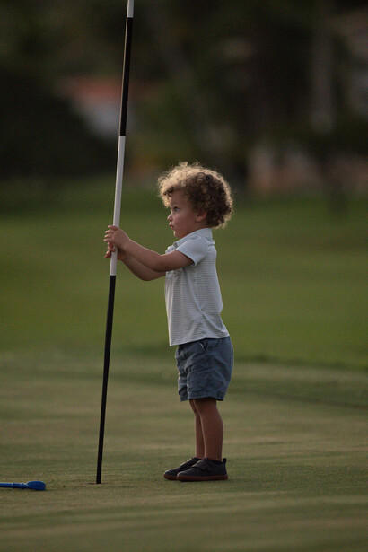 Young child holding a flagstick on a golf green during daytime.