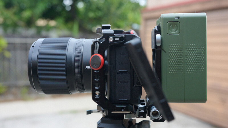 Professional cinema camera mounted on tripod with telephoto lens and green smartphone rig attachment.