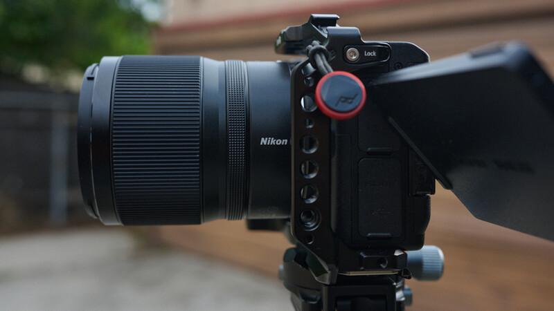 Nikon mirrorless camera with telephoto lens mounted on tripod against blurred outdoor background.
