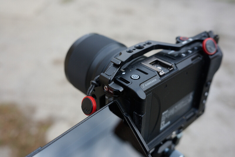 Black cinema camera mounted on a rod with red focus knobs and electronic viewfinder.
