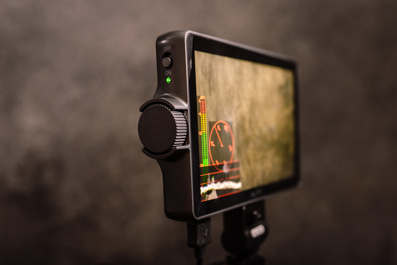 Professional monitor displaying a thermal or infrared image with an external headphone mounted on its side.