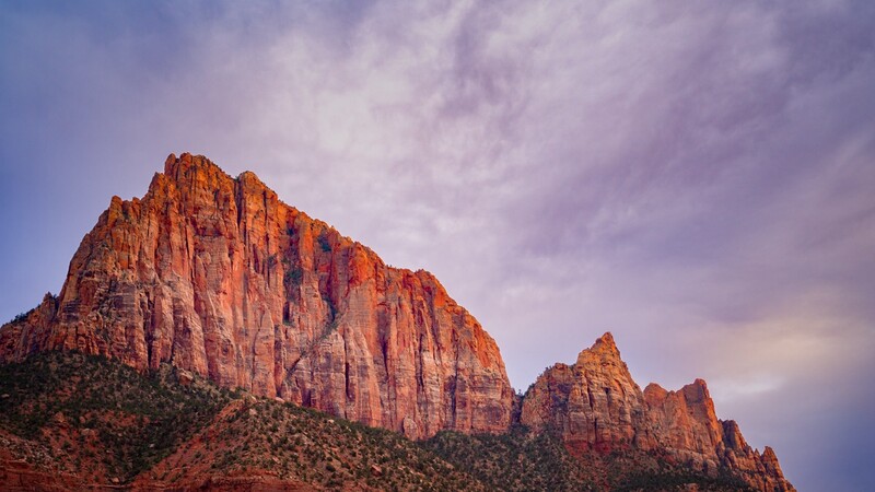 Towering red rock formations with vertical columnar striations under a dramatic purple-tinted sky at dusk.
