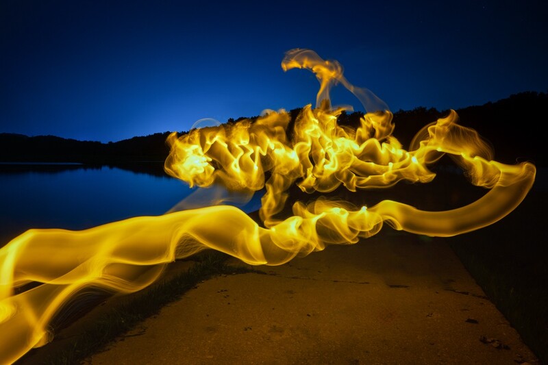 Glowing yellow silk fabric flowing across a dark beach at night with mountains and still water in the background.