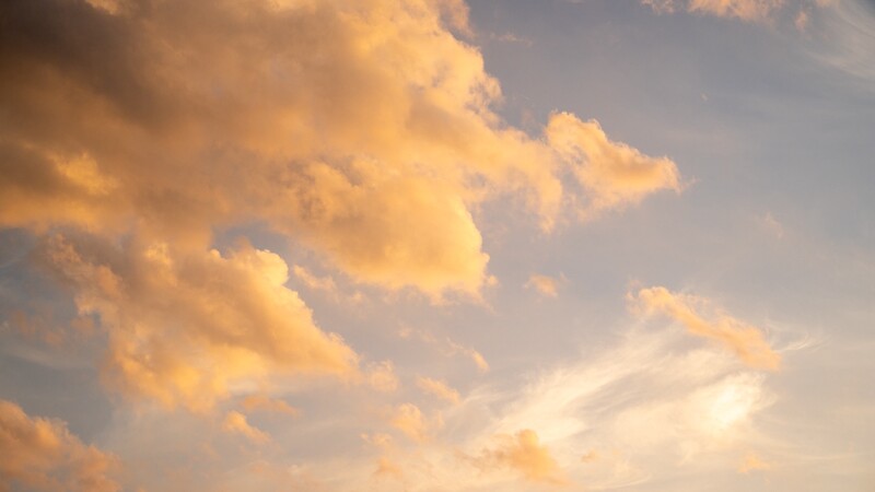 Golden-hour clouds with warm amber and cream tones against a blue sky.