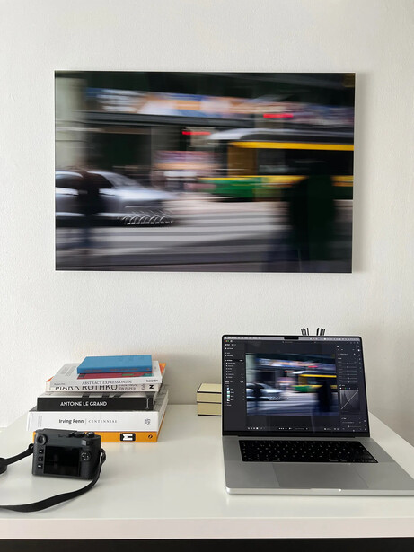 Motion-blurred street scene with cars and yellow bus displayed as framed print above laptop showing the same image.