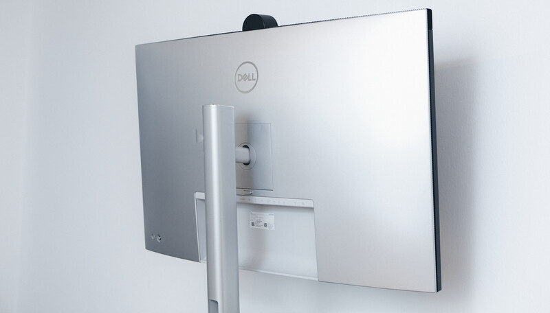 Back view of a Dell all-in-one monitor with silver stand against white wall.