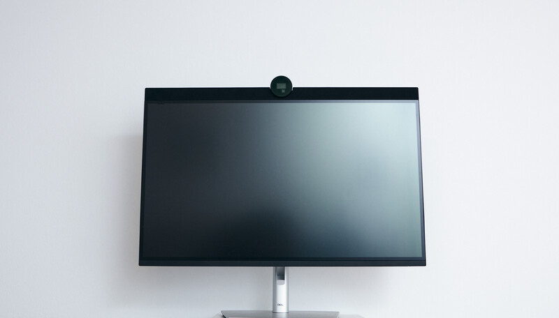 Modern flat-screen monitor mounted on a white wall with a webcam positioned on top of the bezel.