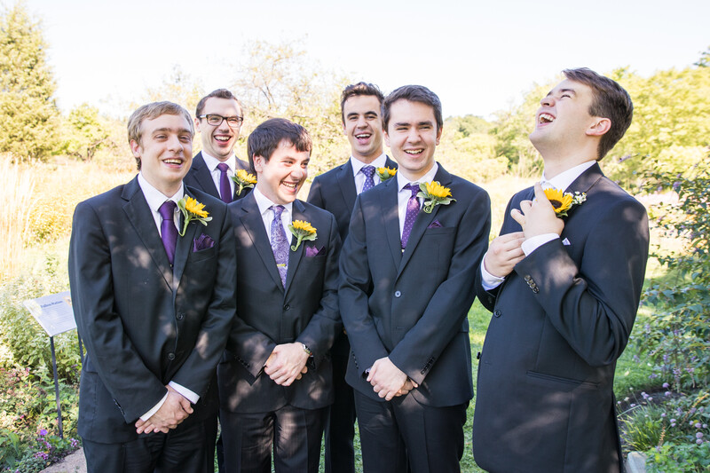Six groomsmen in dark suits with yellow boutonnières standing together outdoors.