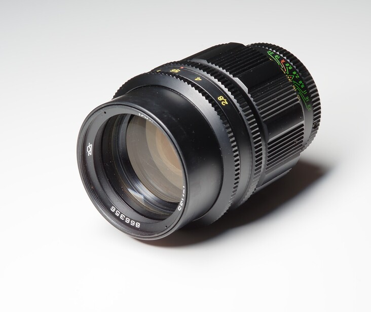 Telephoto cinema lens with focus ring and ribbed barrel against neutral background.