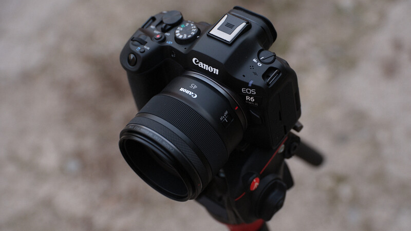 Canon EOS R5 mirrorless camera with RF lens mounted on a tripod head against a concrete surface.