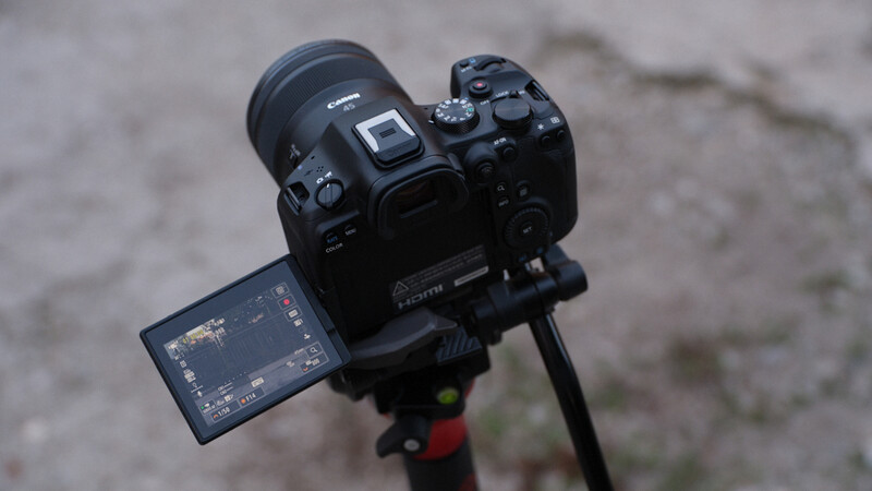 Professional mirrorless camera mounted on tripod with articulating LCD screen deployed and extended lens attached.