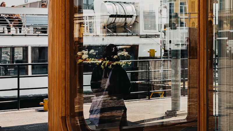 Sunlit urban balcony with wooden frame and glass door overlooking a city street and buildings.
