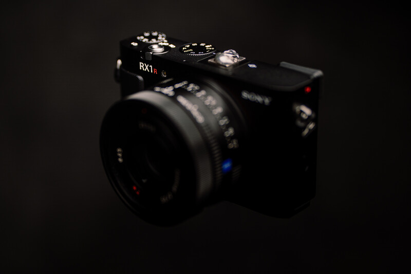 Black mirrorless camera with attached lens against dark background, with blue LED indicator visible.