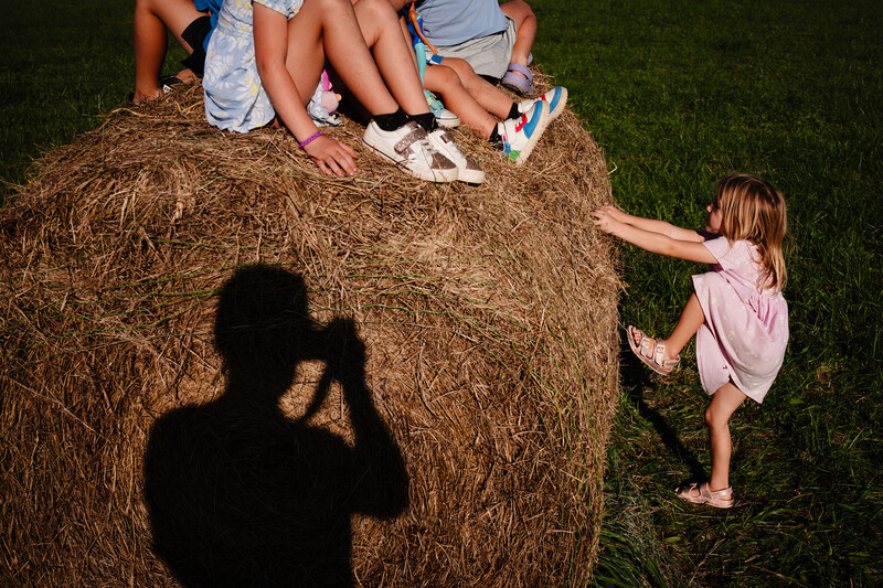 Photographer's shadow visible while shooting children playing on a hay bale outdoors.