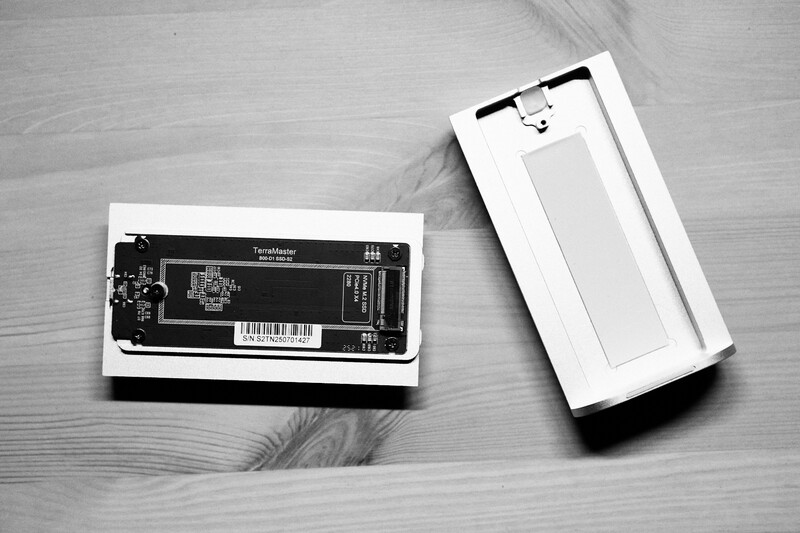 Disassembled smartphone showing internal circuit board and empty white casing on wooden surface.