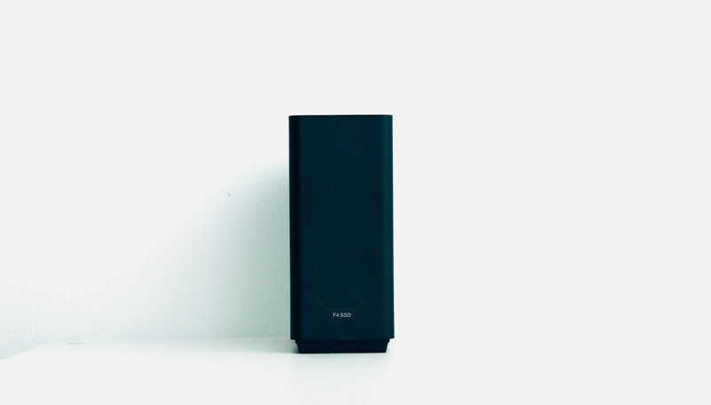 Dark rectangular tower speaker or audio device against a white background with soft shadow.