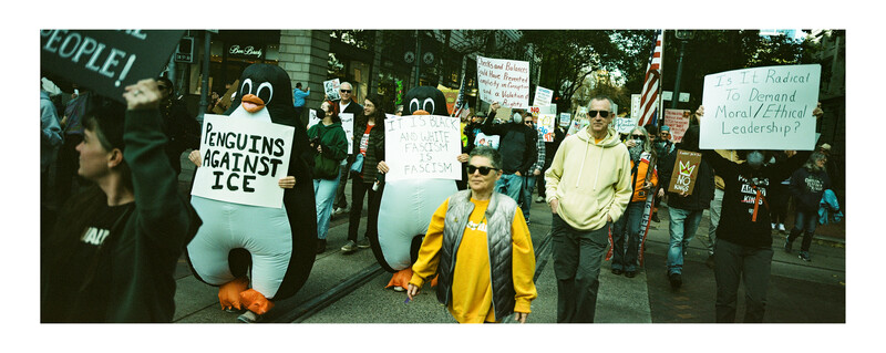 Protesters march down a city street carrying signs and inflatable penguin costumes with climate change messages.