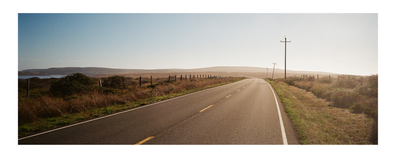 Straight asphalt road stretching toward the horizon through rolling grassland with utility poles lining both sides.