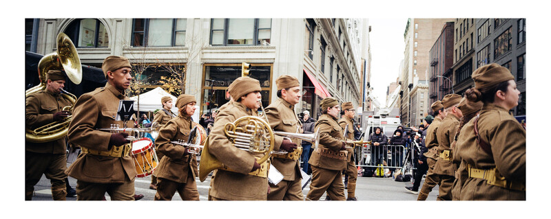 Military marching band in uniform performing on an urban street during daytime parade.
