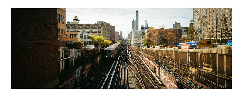 Elevated subway tracks stretching toward a city skyline with tall buildings and autumn foliage.