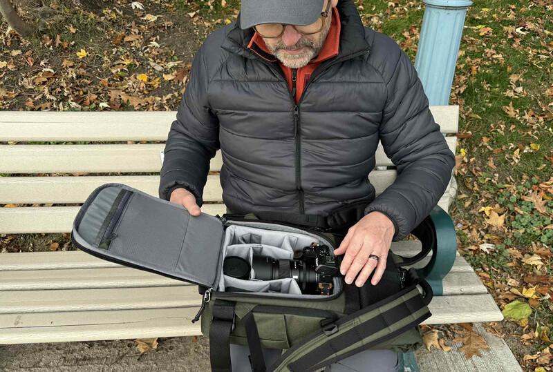 Photographer sitting on a bench organizing camera equipment in a padded gear bag.