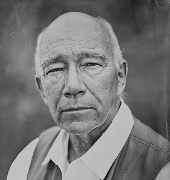 Black and white portrait of an older man with a serious expression, wearing a collared shirt.