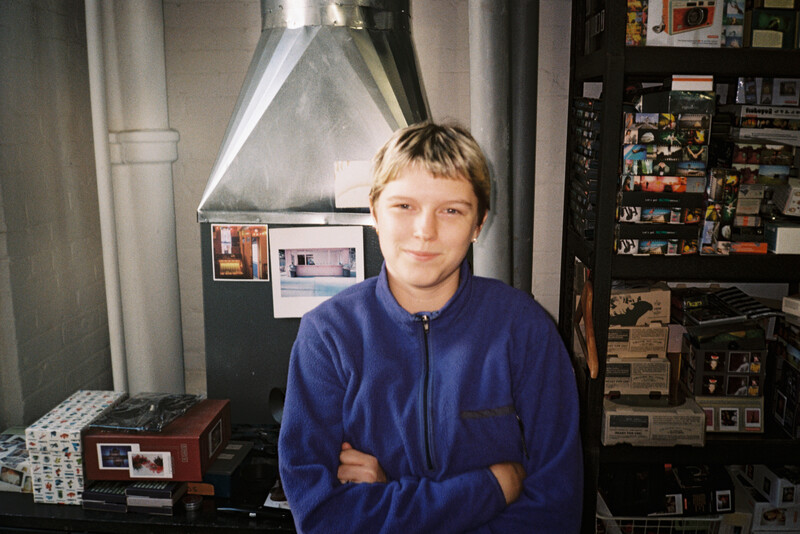 Young person in blue jacket standing in front of photography equipment and lighting setup in studio space.