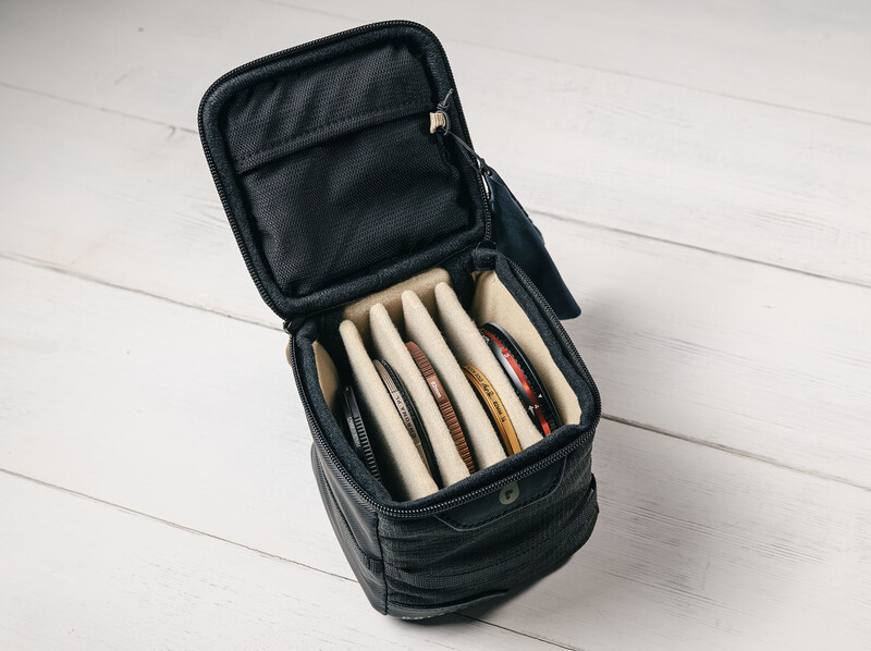 Open black camera bag displaying organized compartments with cream-colored lens cases inside.