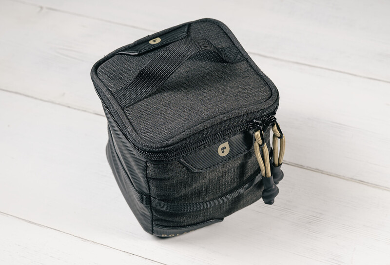 Gray fabric camera bag with top-loading design and carry handle on white wooden surface.