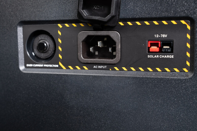 Close-up of a power supply unit's rear panel showing AC input connector, solar charge indicator lights, and overcurrent protection label.