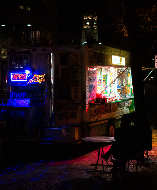 Neon signs and illuminated storefront windows on a dark urban street at night.