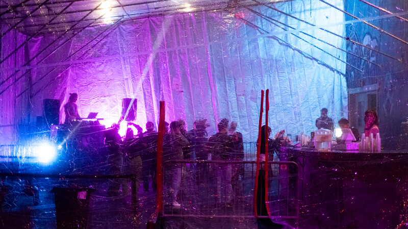 Musicians performing on an elevated stage with vibrant purple and blue neon lighting and layered architectural elements.