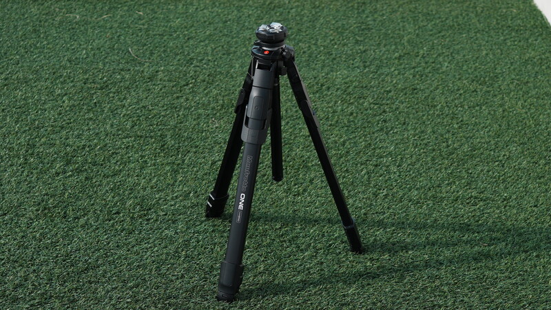Black tripod with ball head mounted on artificial green turf surface.
