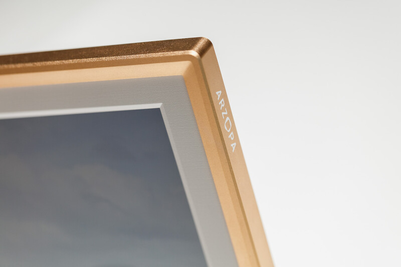 Close-up of a wooden frame corner with gold finish and gray matting against white background.