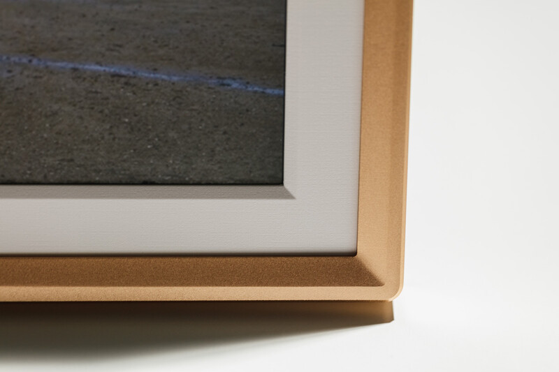 Close-up of layered picture frame corners showing white mat board and natural wood trim against white background.
