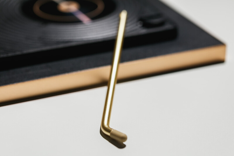 Brass tone stylus resting on a turntable with wooden base and black platter.