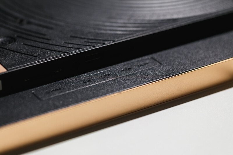 Close-up of a vinyl record edge with wooden tonearm resting against the black grooved surface.