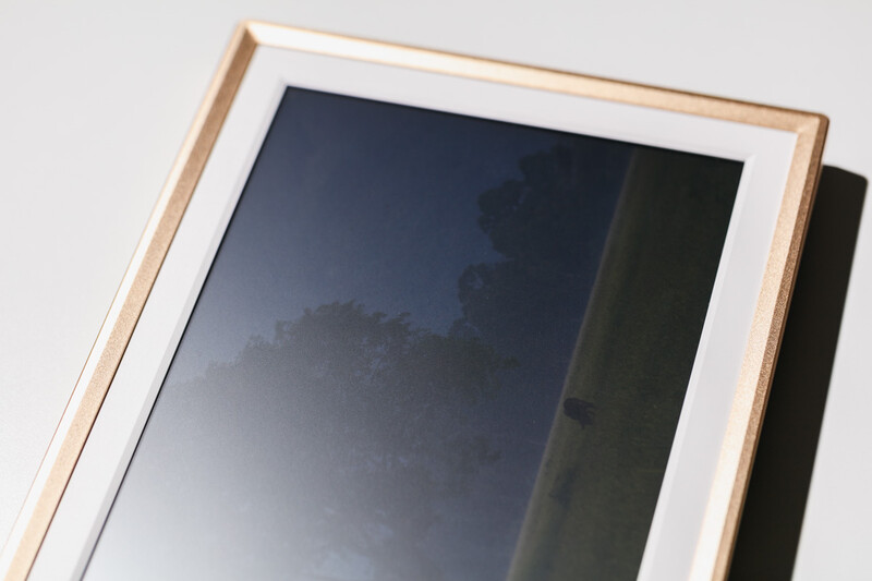 Wooden picture frame with white mat and glass covering a dark landscape photograph.