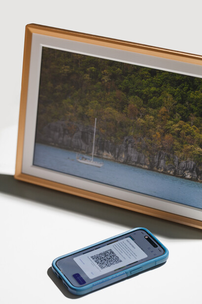 Wooden-framed landscape photograph displaying a serene waterside forest scene positioned next to a smartphone with QR code on white surface.