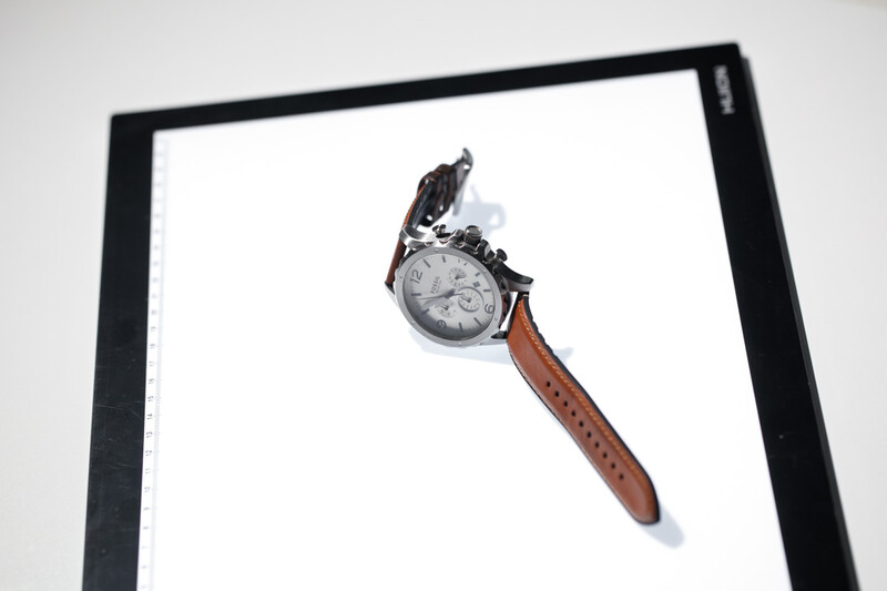 Wristwatch with brown leather strap and dark face displayed on white background with black frame border.