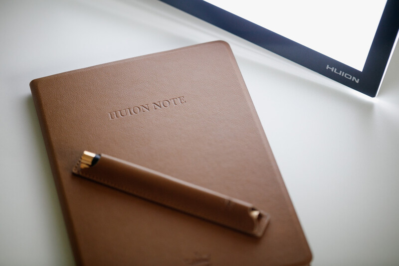 Tan leather notebook with embossed text and a wooden pen resting diagonally across the cover.
