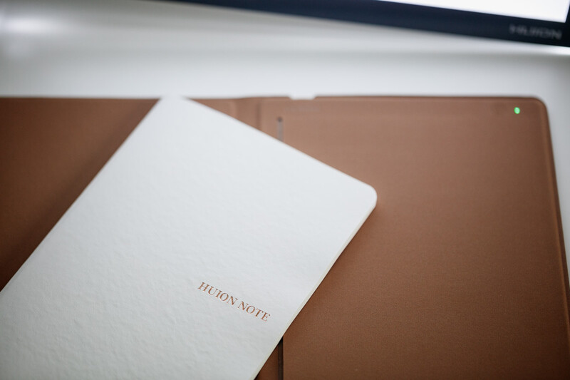 White notebook with embossed text resting on a tan leather surface next to a brown clipboard.