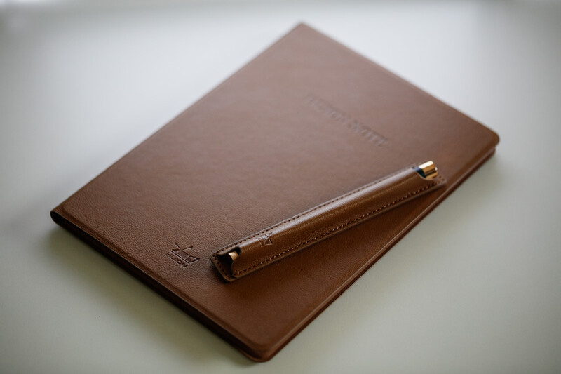 Brown leather notebook with an attached pen on white surface.